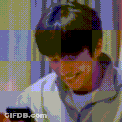 A Man Is Smiling And Looking At His Cell Phone . GIF