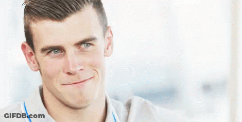 A Man Is Smiling And Making A Funny Face While Wearing A Grey Shirt . GIF