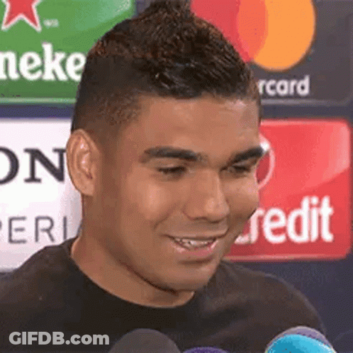 A Man Is Smiling And Talking Into A Microphone While Standing In Front Of A Heineken Sign . GIF
