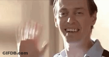 A Man Is Smiling And Waving His Hand At The Camera . GIF