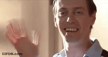 A Man Is Smiling And Waving His Hand In Front Of A Window . GIF