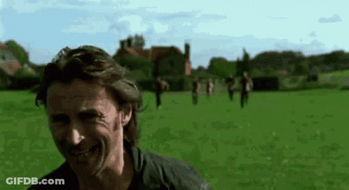 A Man Is Smiling In A Field With A Group Of People Walking In The Background . GIF