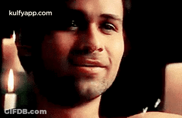 A Man Is Smiling In Front Of A Candle And Looking At The Camera . GIF