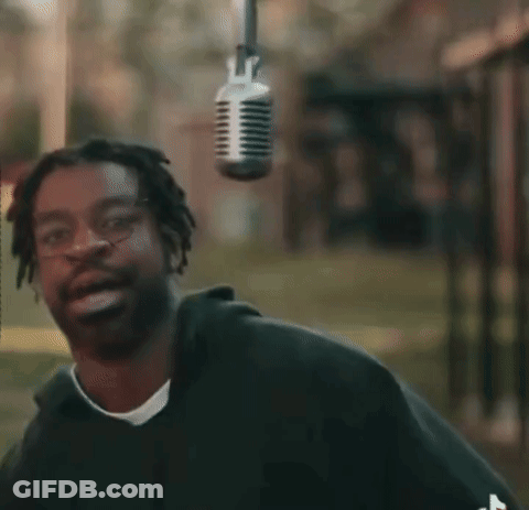 A Man Is Smiling In Front Of A Microphone Hanging From The Ceiling GIF