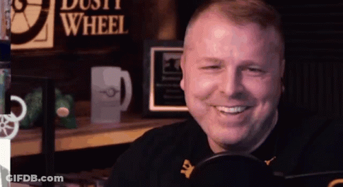A Man Is Smiling In Front Of A Microphone In Front Of A Sign That Says Dust Wheel GIF