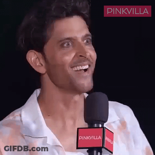 A Man Is Smiling In Front Of A Microphone That Says Pinkvilla On It GIF