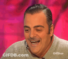 A Man Is Smiling In Front Of A Pink Background With Gifstar On The Bottom GIF