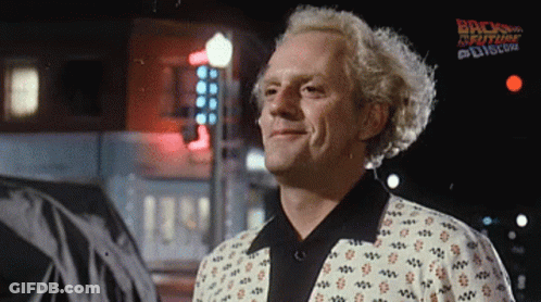 A Man Is Smiling In Front Of A Sign That Says Back To The Future On It GIF