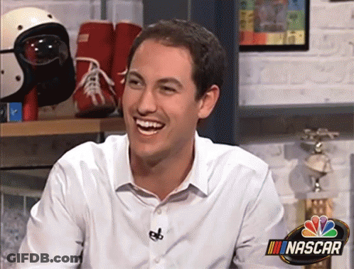 A Man Is Smiling In Front Of A Sign That Says Nascar GIF