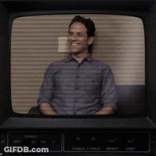 A Man Is Smiling In Front Of A Tv Screen That Says Hold V Hold GIF