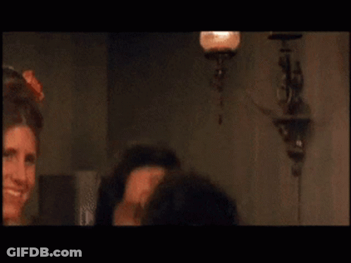 A Man Is Smiling In Front Of A Woman In A Room GIF