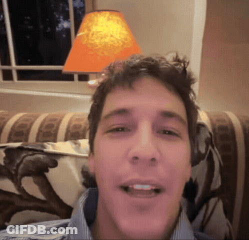 A Man Is Smiling In Front Of An Orange Lamp GIF