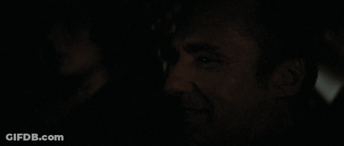 A Man Is Smiling In The Dark With A Woman In The Background GIF