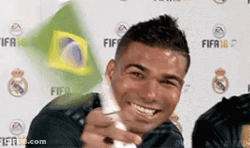 A Man Is Smiling While Holding A Wii Controller In Front Of A Brazilian Flag . GIF