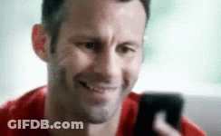 A Man Is Smiling While Looking At His Phone GIF