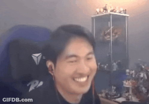 A Man Is Smiling While Sitting In A Chair In Front Of A Display Case Of Figurines . GIF