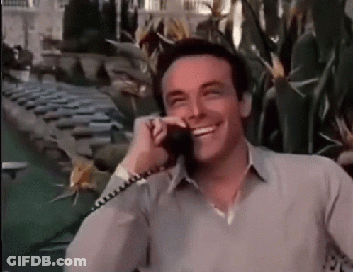 A Man Is Smiling While Talking On A Phone In Front Of A Pool . GIF