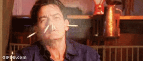 A Man Is Smoking A Cigarette In A Kitchen With Smoke Coming Out Of His Nose . GIF