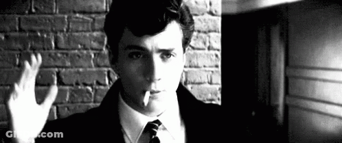 A Man Is Smoking A Cigarette In Front Of A Brick Wall . GIF