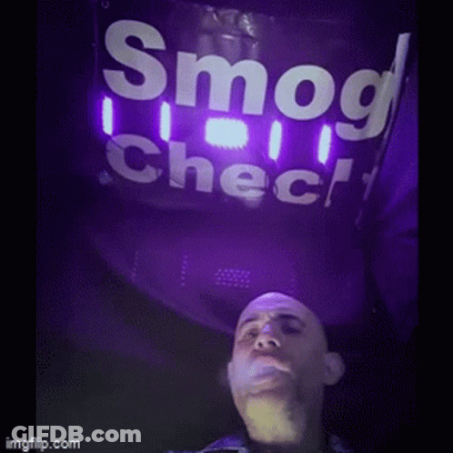 A Man Is Smoking A Cigarette Under A Sign That Says Smog Check GIF