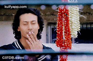 A Man Is Smoking A Cigarette While Looking Through A Window At Flowers . GIF
