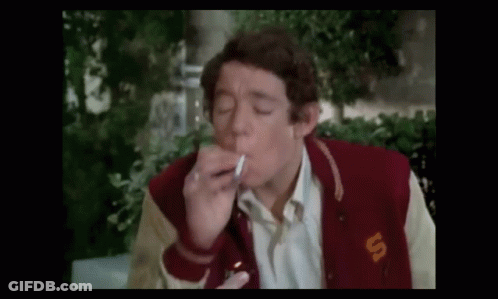 A Man Is Smoking A Cigarette While Wearing A Varsity Jacket . GIF
