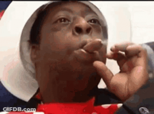 A Man Is Smoking A Cigarette With His Fingers In His Mouth . GIF
