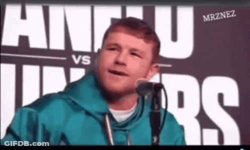 A Man Is Speaking Into A Microphone In Front Of A Sign That Says Alvarez GIF