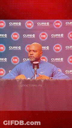 A Man Is Speaking Into A Microphone In Front Of A Wall That Says Cure GIF