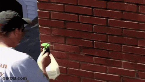 A Man Is Spraying A Brick Wall With A Sprayer GIF