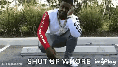 A Man Is Squatting Down In A Parking Lot With The Words Shut Up Whore Written Below Him . GIF