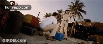 A Man Is Squatting Down In Front Of A Police Officer On A Beach . GIF