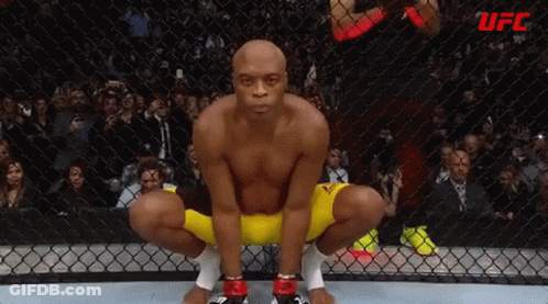 A Man Is Squatting In A Boxing Ring With A Crowd Watching . GIF