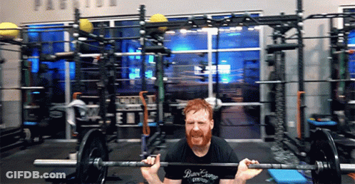 A Man Is Squatting With A Barbell In A Gym Wearing A Shirt That Says Bear Earring GIF