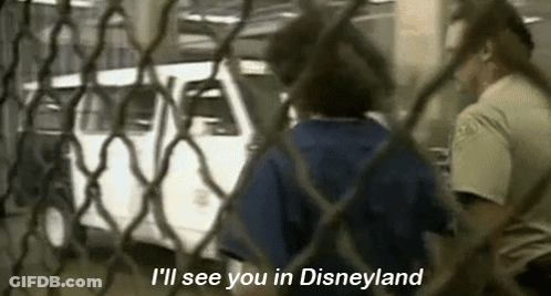 A Man Is Standing Behind A Chain Link Fence Talking To A Woman Behind It . GIF