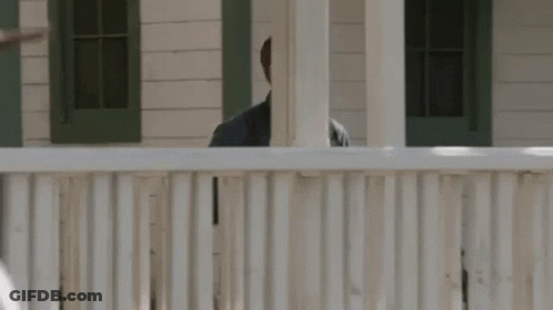 A Man Is Standing Behind A White Fence Looking Over It . GIF