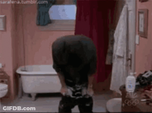 A Man Is Standing In A Bathroom With A Bathtub In The Background . GIF