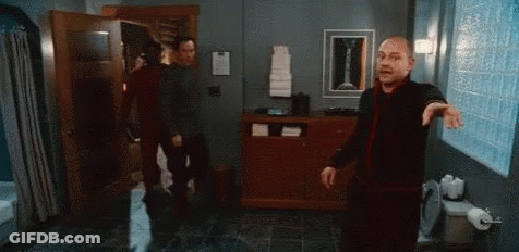 A Man Is Standing In A Bathroom With Another Man . GIF