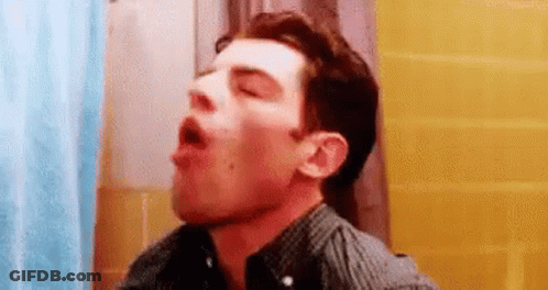 A Man Is Standing In A Bathroom With His Mouth Open And His Eyes Closed . GIF