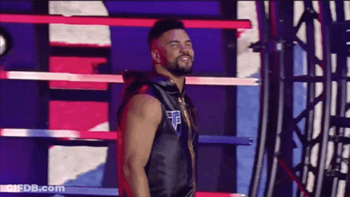 A Man Is Standing In A Boxing Ring Wearing A Black Vest And Smiling . GIF