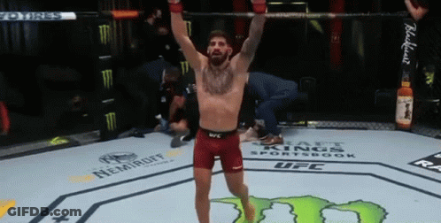 A Man Is Standing In A Boxing Ring With His Arms Up In The Air . GIF