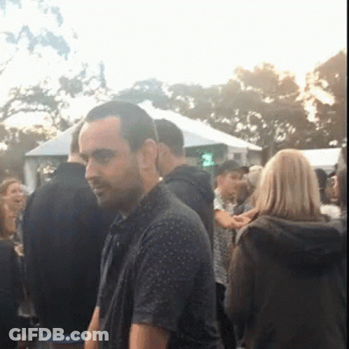 A Man Is Standing In A Crowd Of People With A Green Light In The Background GIF