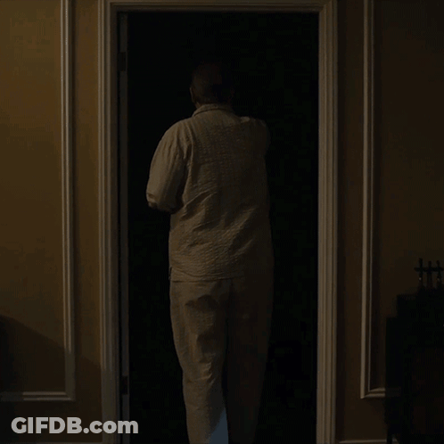 A Man Is Standing In A Dark Closet With A Lamp On GIF