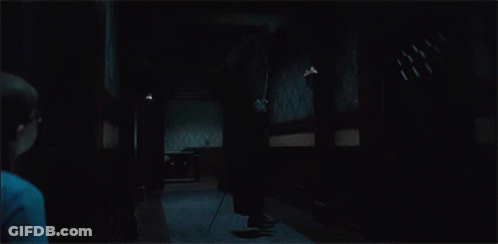 A Man Is Standing In A Dark Hallway Holding A Cane GIF