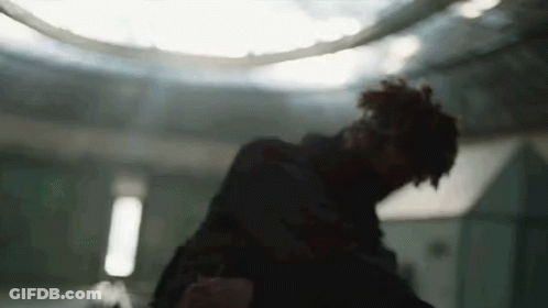 A Man Is Standing In A Dark Room With A Ceiling Light In The Background . GIF