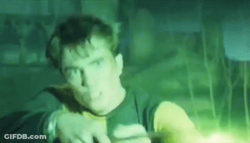 A Man Is Standing In A Dark Room With A Green Light Coming Out Of His Hand . GIF