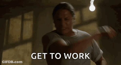 A Man Is Standing In A Dark Room With A Light Bulb Hanging From The Ceiling And Says `` Get To Work '' . GIF
