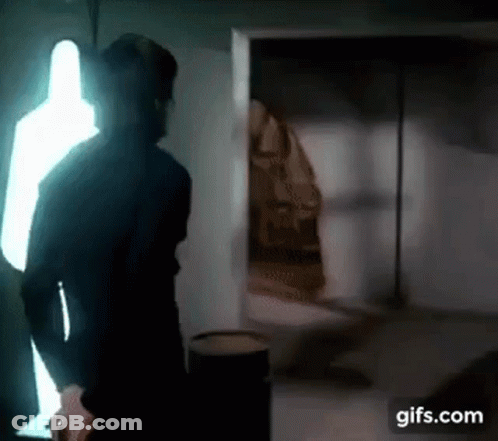 A Man Is Standing In A Dark Room With A Light Shining Through The Window . GIF