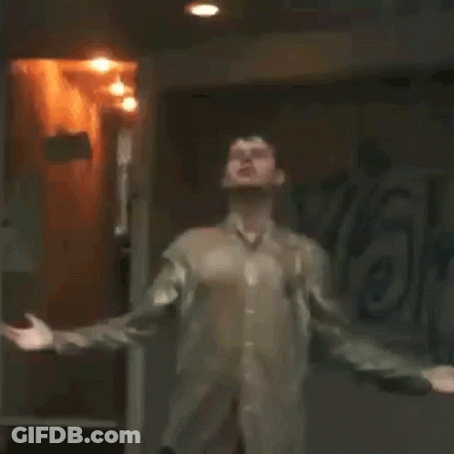 A Man Is Standing In A Dark Room With His Arms Outstretched And Looking Up . GIF
