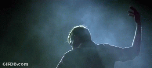 A Man Is Standing In A Dark Room With His Arms Outstretched In The Air . GIF